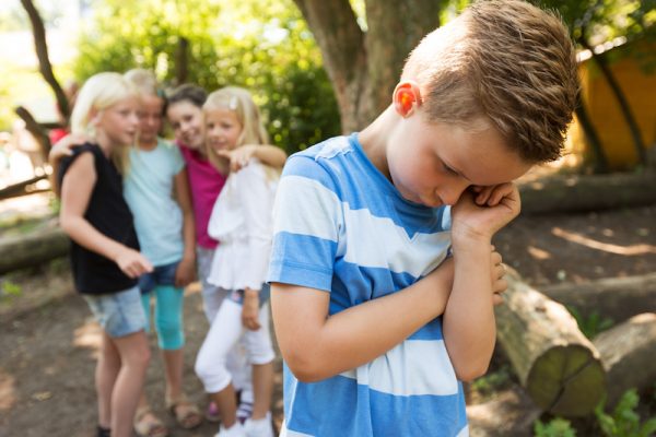 Junge wird aus Gruppe ausgeschlossen. Mädchen zeigen mit dem Finger auf ihn.